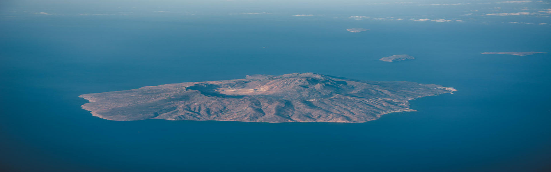 Aerial view over Nisyros island, Greece. Nisyros is a volcanic Greek island and municipality located in the Aegean Sea. It is part of the Dodecanese group of islands, situated between the islands of Kos and Tilos.
Its shape is approximately round, with a diameter of about 8 km and an area of 41.6 km2. Several other islets are found in the direct vicinity of Nisyros, the largest of which is Gyali, with a population of 22 citizens.